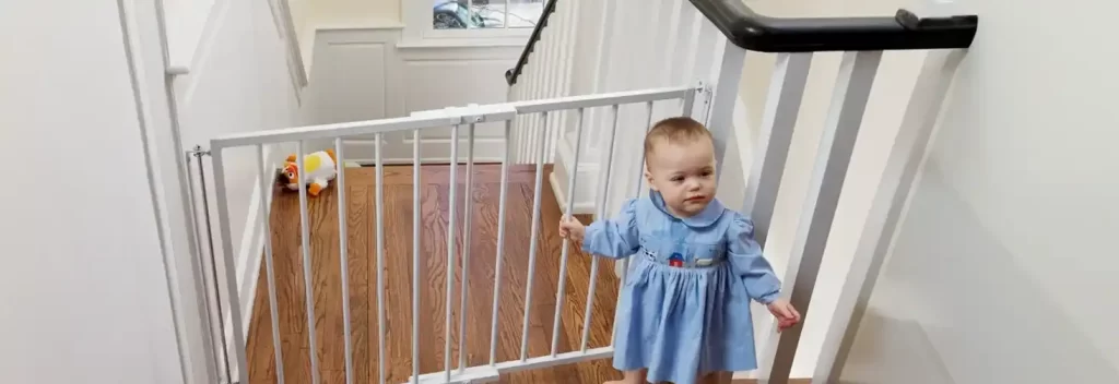 A toddler standing safely behind the Cardinal Gates Stairway Special Safety Gate installed at the top of a staircase. The gate is securely mounted, providing a robust barrier to prevent access to the stairs. This childproof gate is ideal for ensuring staircase safety, offering parents peace of mind while their little explorer moves around the home. The clean design and durable construction make it a top choice for babyproofing staircases and other high-risk areas.