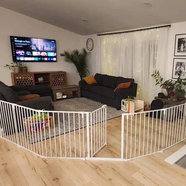 The Regalo Super Wide Baby Gate and Play Yard set up in a living room, creating a secure play area for a child. The gate is configured to fit the space, demonstrating its versatility in covering large areas. Ideal for babyproofing open floor plans, this childproof gate provides a safe environment for your little one to play and explore.