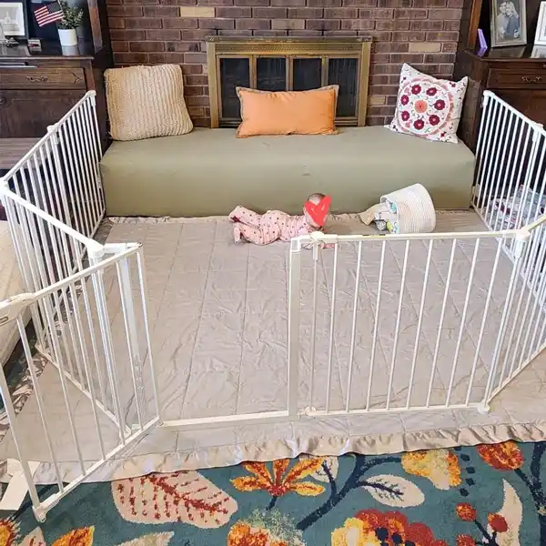 The Regalo Super Wide Baby Gate and Play Yard used as a barrier around a fireplace, providing a safe distance between the child and the hearth. The gate is configured to fit the space, demonstrating its versatility and effectiveness in childproofing various areas of the home. This best safety gate is ideal for ensuring your little explorer stays safe in high-risk areas.