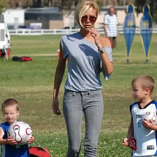 Victoria Beckham epitomizes casual soccer mom style in this effortless outfit. She is dressed in a relaxed off-the-shoulder gray top paired with slim-fit gray jeans. Her look is completed with stylish sunglasses and minimal accessories, making it perfect for a laid-back day at the soccer field. This ensemble combines comfort and chicness, ideal for moms who want to look stylish while staying comfortable.