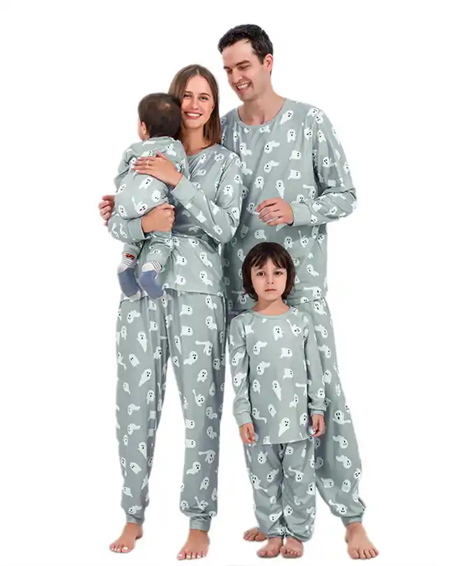 Family dressed in matching gray Halloween pajamas with white ghost patterns, including mom, dad, a toddler, and a baby, all smiling and posing together.