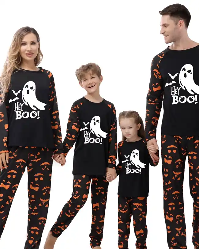 Family dressed in matching Halloween pajamas featuring black tops with a white ghost and 'Hey Boo!' text, along with black and orange bottoms with jack-o'-lantern faces. The family includes mom, dad, and two children, all holding hands and smiling.