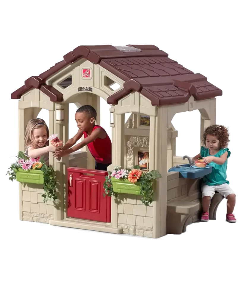 Step2 Neat & Tidy Cottage Playhouse with three children playing, featuring a red door, flower boxes, and an outdoor sink.