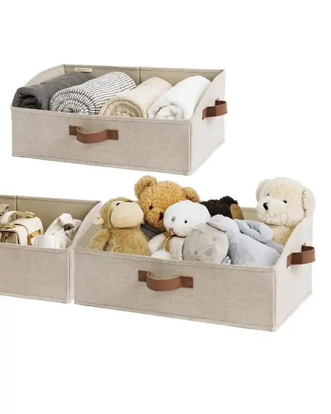 A set of trapezoid-shaped canvas storage boxes with handles, filled with stuffed animals, blankets, and baby items, providing a soft and sturdy toy storage solution.