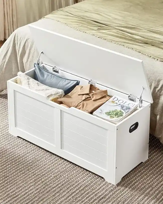 A white toy storage chest with a hinged lid, partially open, revealing neatly stored toys and items, providing a discreet and stylish toy storage solution.