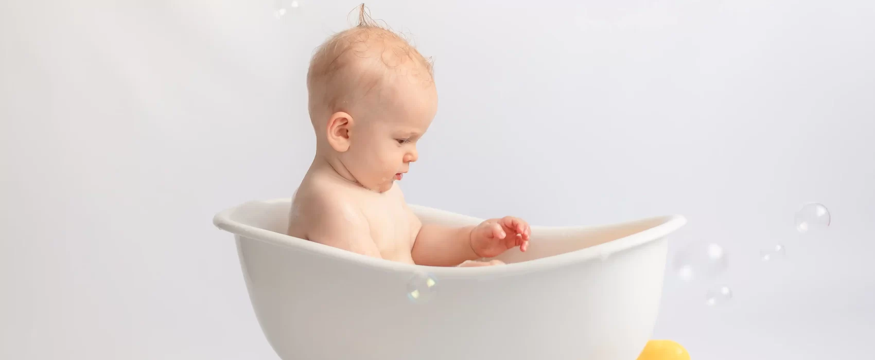 An adorable baby sitting in a baby bath tub, surrounded by bubbles, enjoying a relaxing and fun bath time.