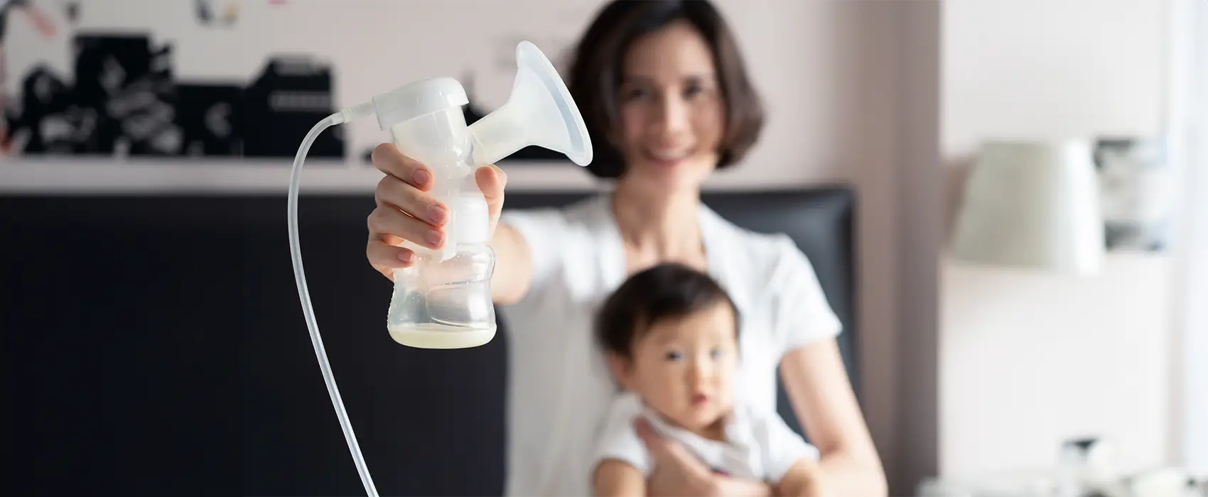 Mom using a breast pump while holding her baby, showcasing the essentials for exclusively pumping moms.