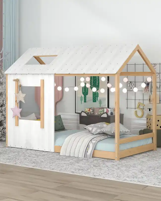 A beautifully designed Montessori floor bed with a house-shaped roof, featuring string lights for a cozy ambiance. The toddler floor bed has a wooden frame with a white roof and open sides, creating a playful and inviting space for children. The room is decorated in a modern style, perfect for fostering independence and imaginative play.