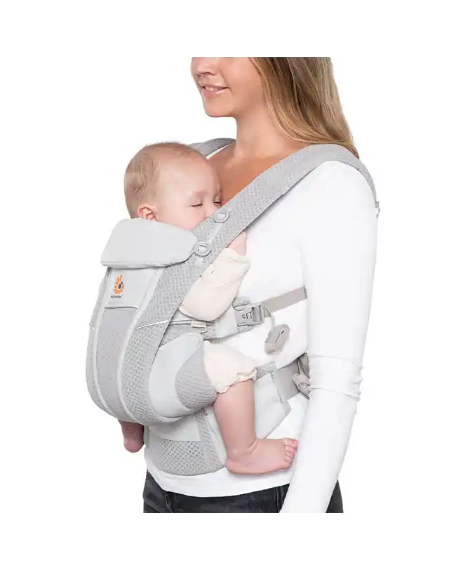  A woman carrying an infant in the Ergobaby Omni Breeze Carrier, an essential infant travel accessory for comfort and versatility.