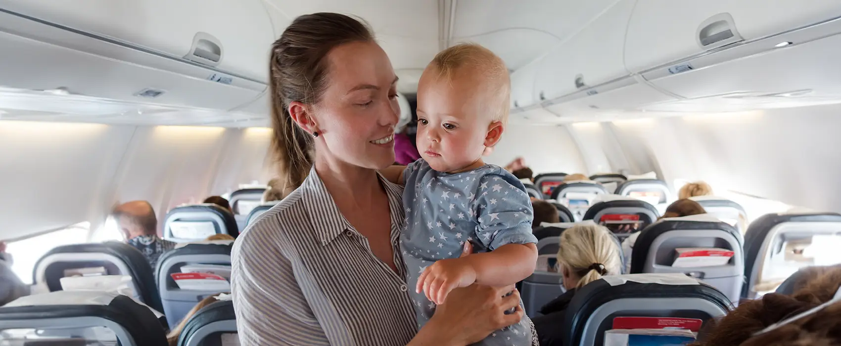 A mother holding her baby on an airplane, illustrating the importance of infant travel essentials for a smooth journey.