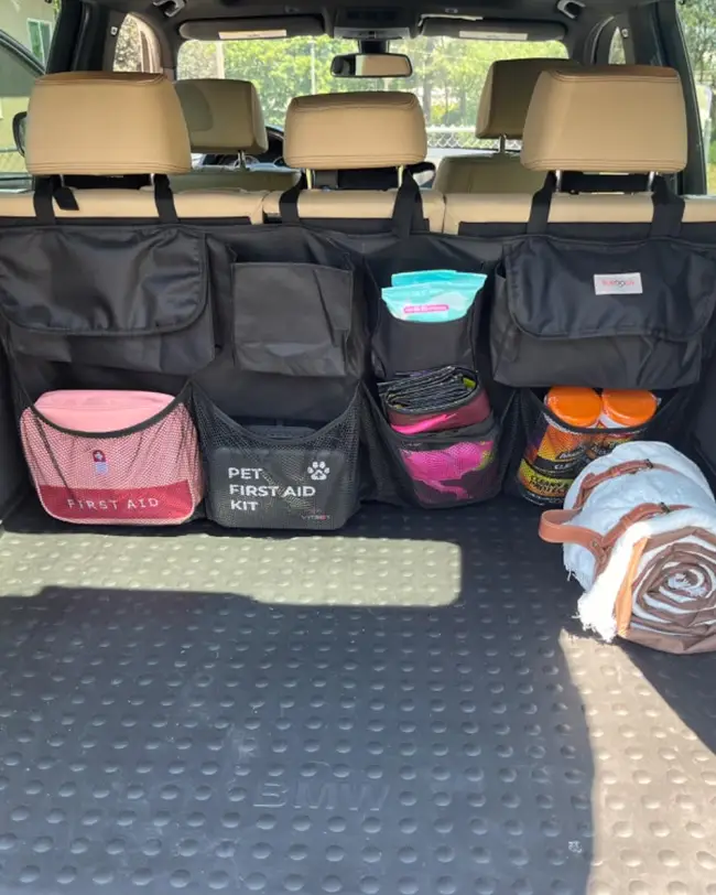 A hanging trunk organizer attached to the back of the seats, storing first aid kits, blankets, and wipes for better car organization.