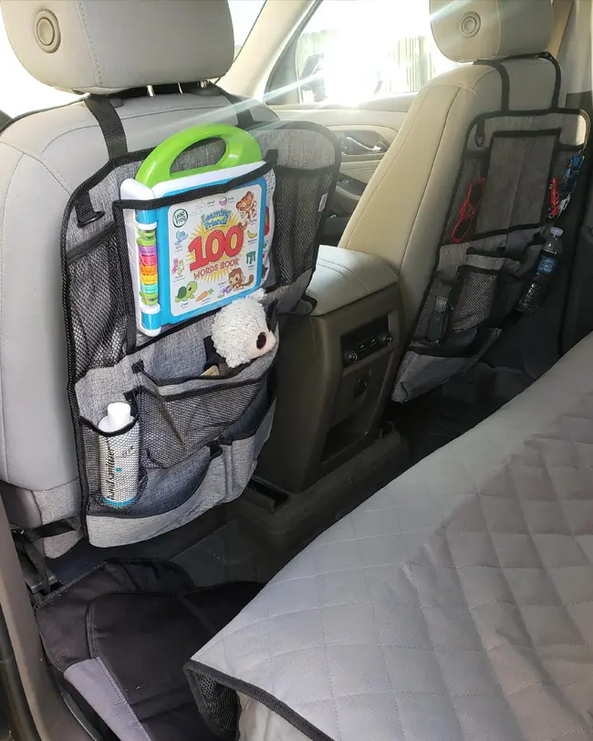 A backseat car organizer with pockets holding toys, books, and other essentials for improved car organization and easy access during trips.