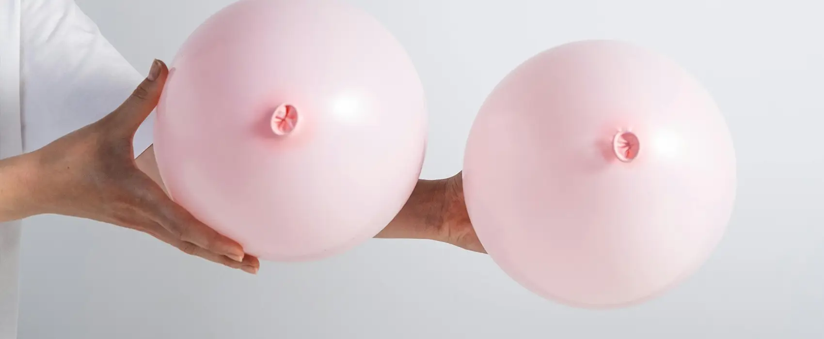 Two pink balloon models representing breasts, used to visually explain a power pumping schedule for increasing milk supply.