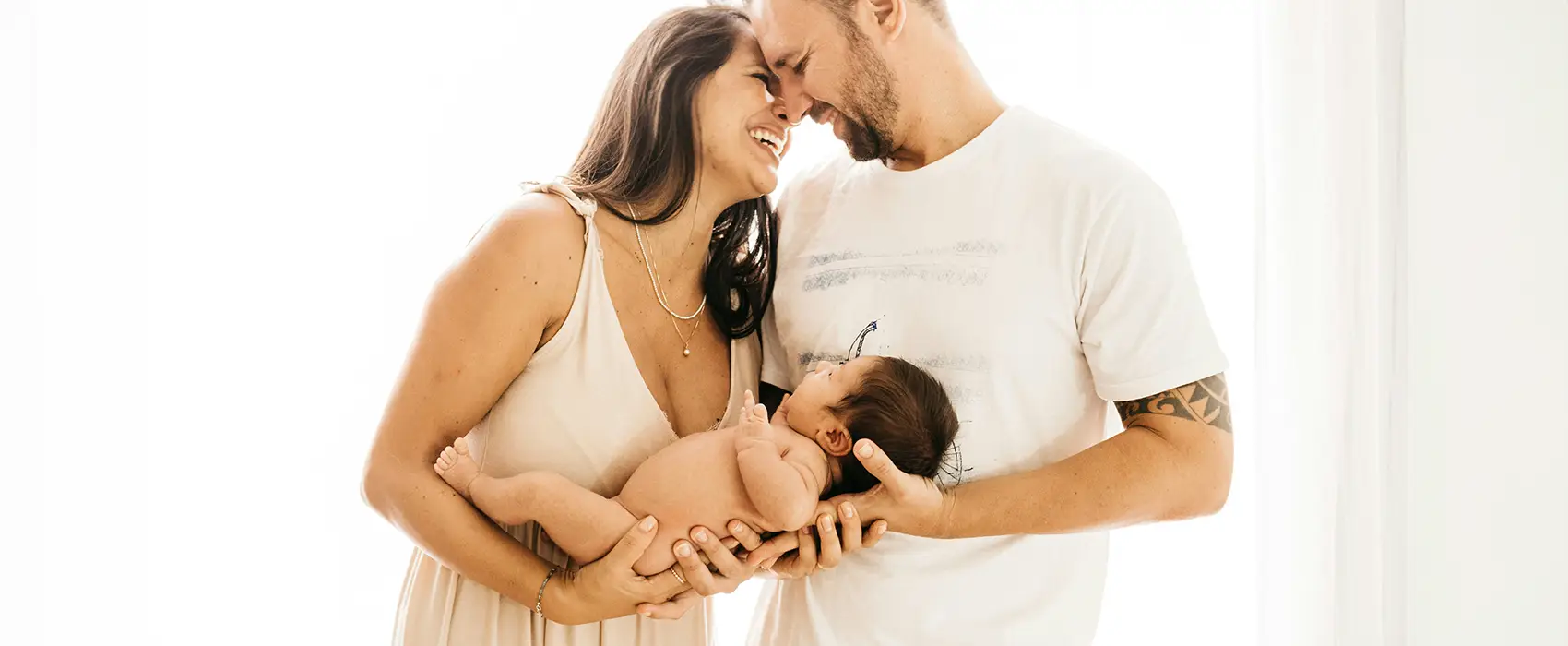 A joyful couple lovingly holding their newborn baby together, embodying heartfelt advice for new parents in a softly lit, warm setting.