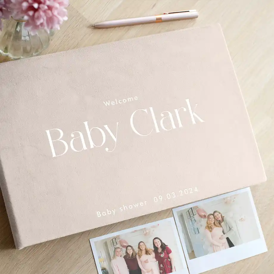 Elegant baby shower guest book with 'Welcome Baby Clark' and a light blush cover, accompanied by Polaroid pictures from the event.