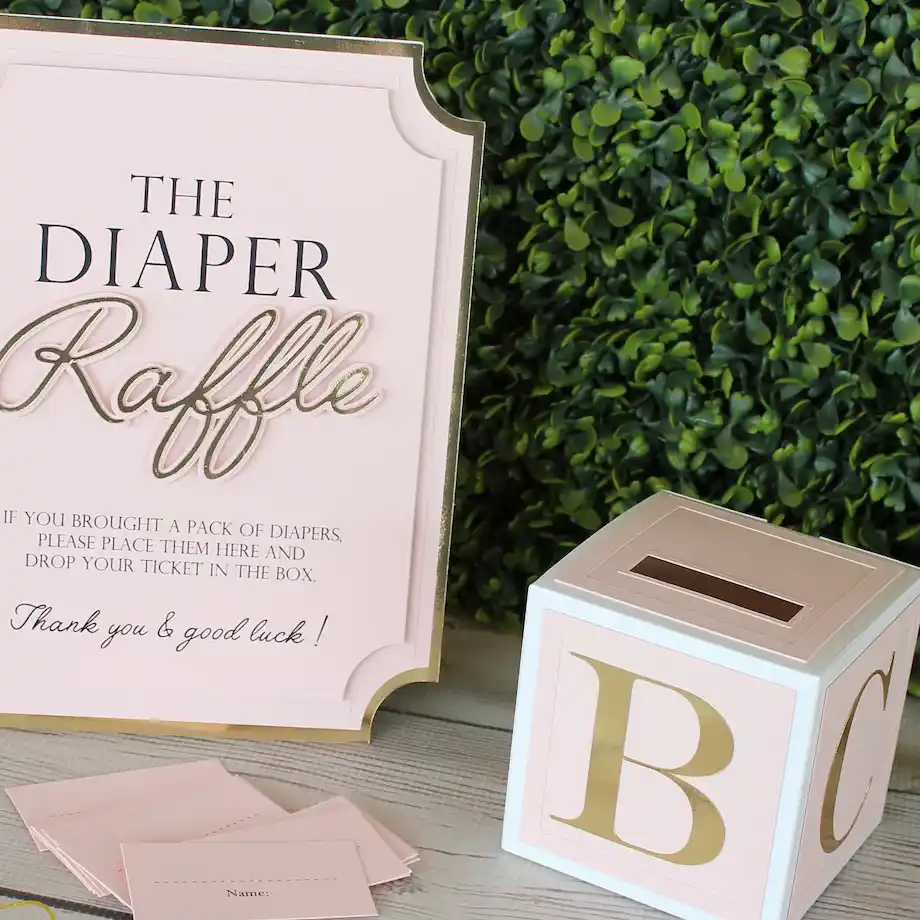 A pink and gold diaper raffle sign with a matching ticket box, perfect for a baby shower game setup.