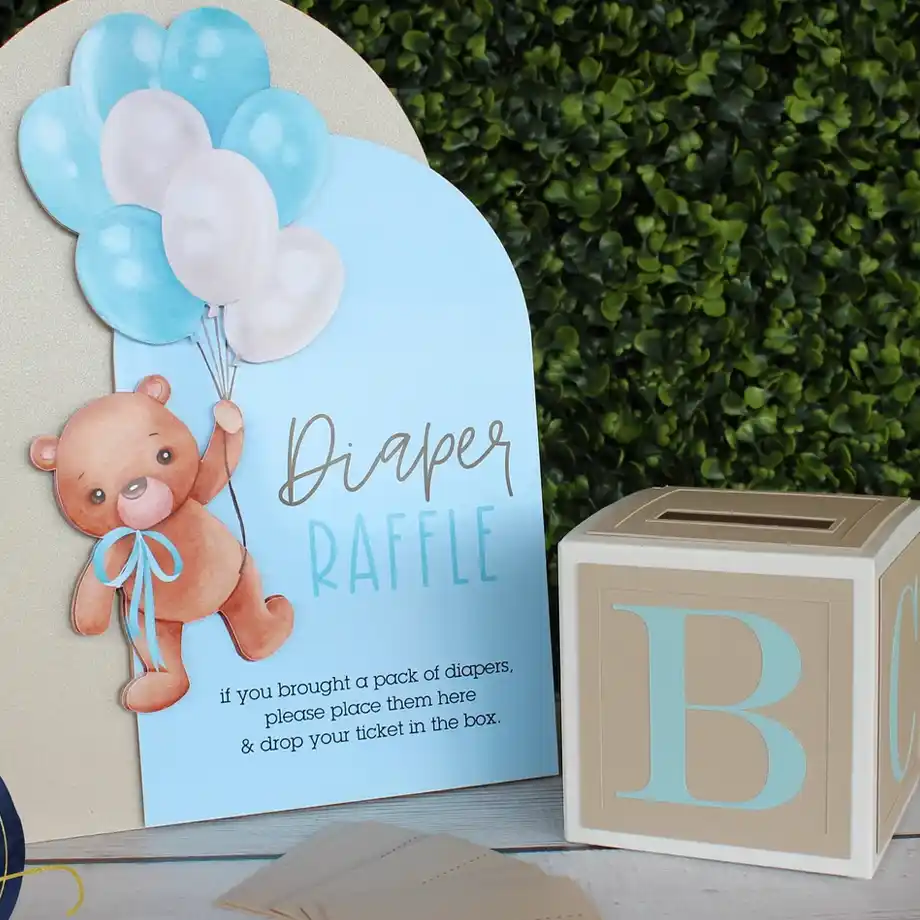 A blue diaper raffle sign with a teddy bear holding balloons and a matching ticket box, perfect for a baby shower game.