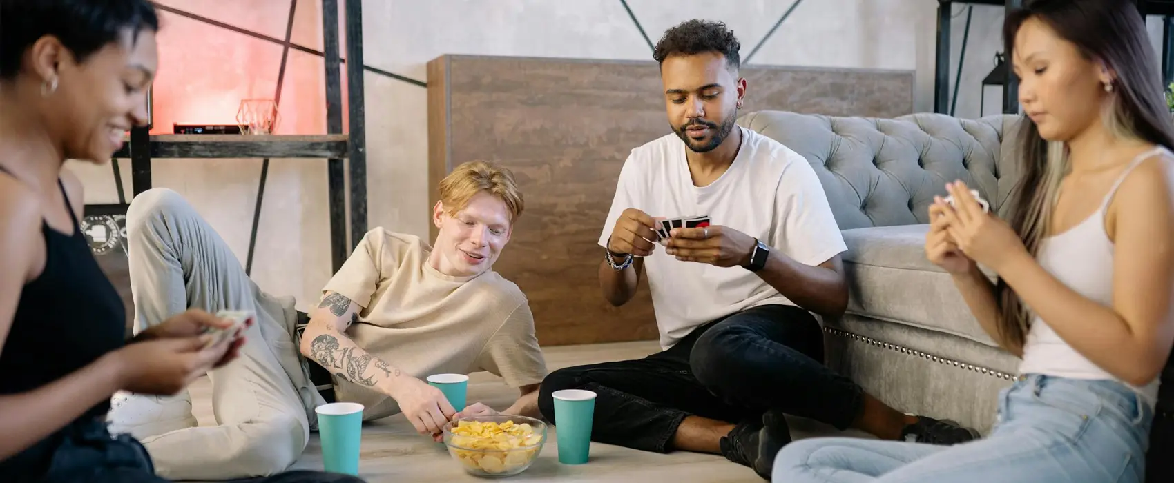 A group of friends sitting on the floor and couch, enjoying a relaxed evening of party games for adults with snacks and drinks nearby.