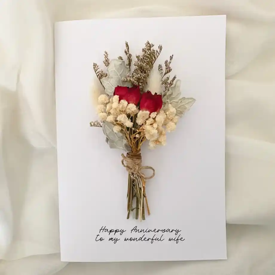 A beautiful anniversary card featuring a delicate bouquet of dried flowers tied with twine and the handwritten message "Happy Anniversary to my wonderful wife," offering inspiration for thoughtful anniversary quotes for a wife.