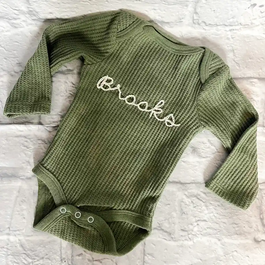 Adorable custom hand-embroidered long-sleeve baby bodysuit, perfect for a thoughtful and unique baby shower gift idea. Features delicate, personalized stitching on soft fabric for comfort and charm.