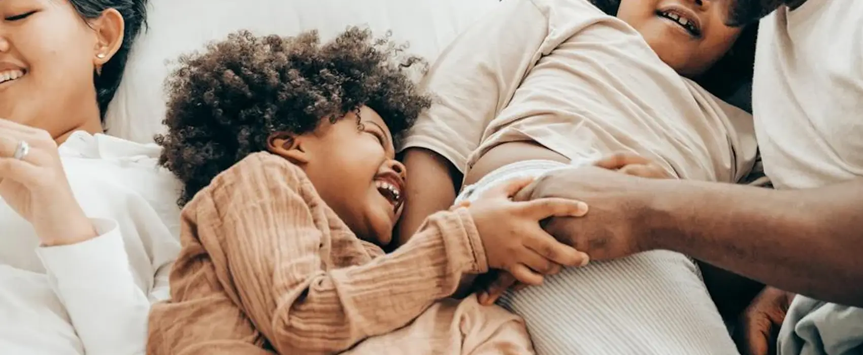 A happy family laughing together on a bed, showcasing the joy of sharing the best kid jokes.