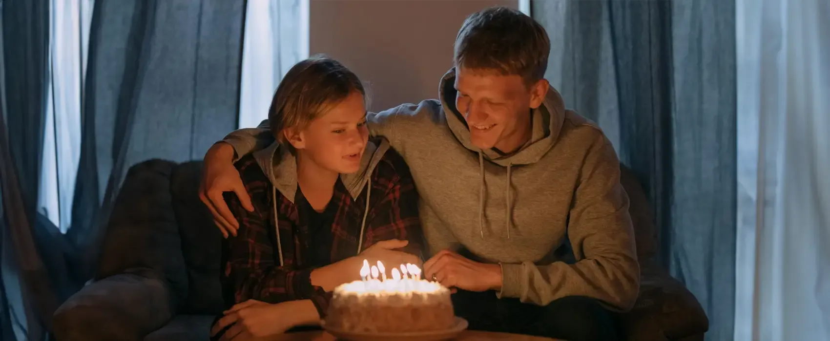 A man in a black and red plaid jacket sitting in front of a birthday cake, celebrating with a joyful moment, ideal for sharing heartfelt birthday wishes for brother.