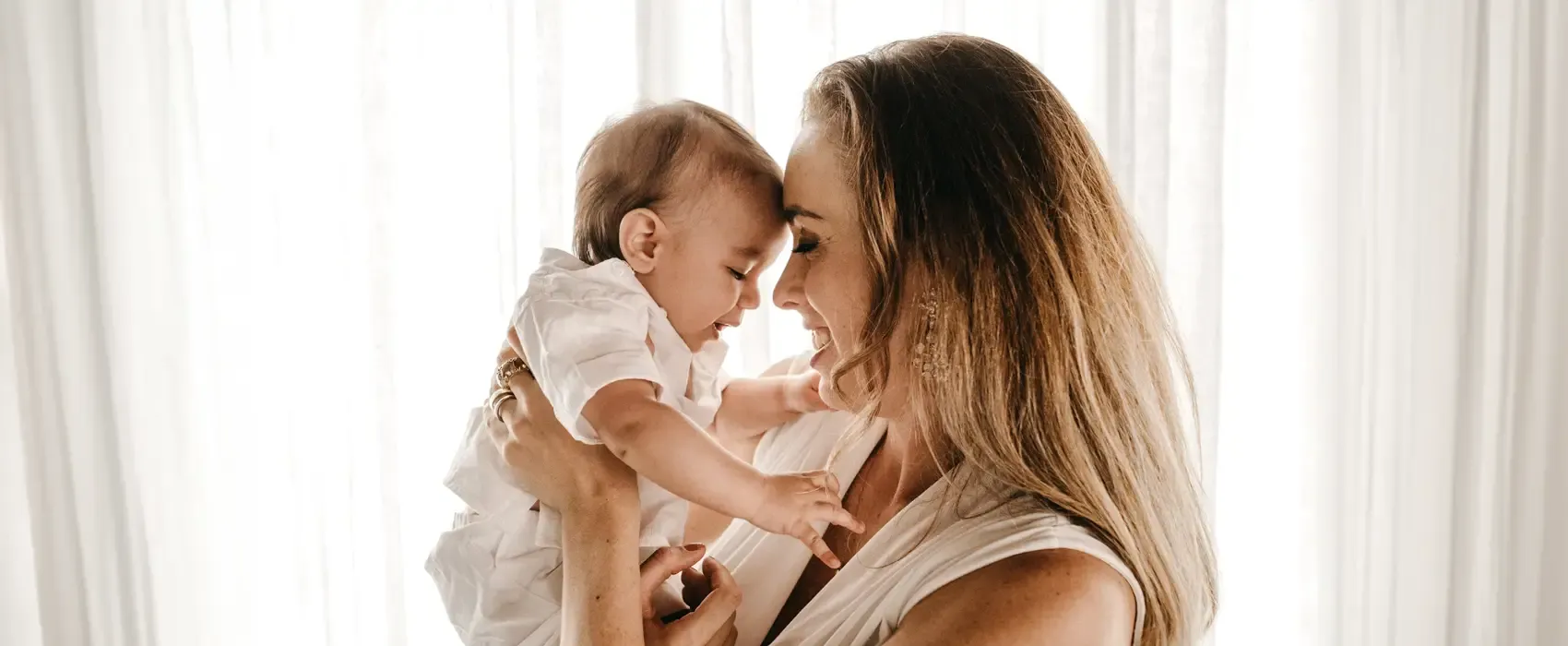 A joyful mother shares a tender moment with her baby daughter, smiling warmly in a light-filled room. This image beautifully represents the theme of "Mother Daughter Quotes" and the unbreakable bond they share.