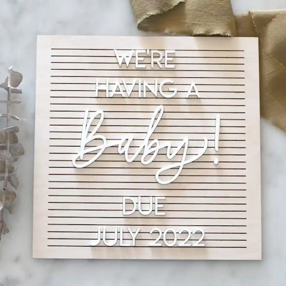 A custom faux wood letter board with baby announcement details, surrounded by neutral decor, offering a modern and personalized way to share pregnancy news.