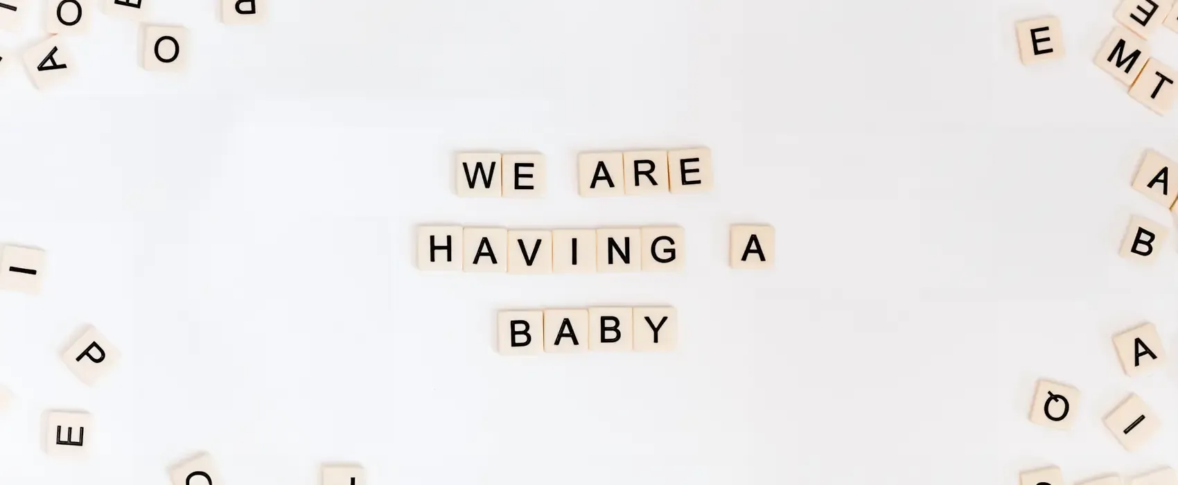 Scrabble tiles spelling out "We are having a baby" on a white background, a fun and creative pregnancy announcement idea.