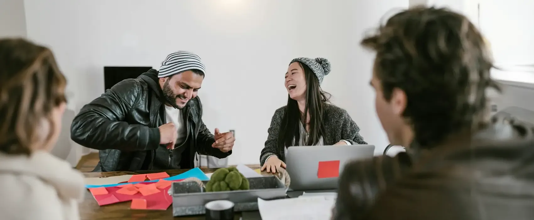 A group of friends laughing and having fun around a table while brainstorming creative two truths and a lie ideas. Includes colorful sticky notes and a laptop, creating a lively and engaging atmosphere.