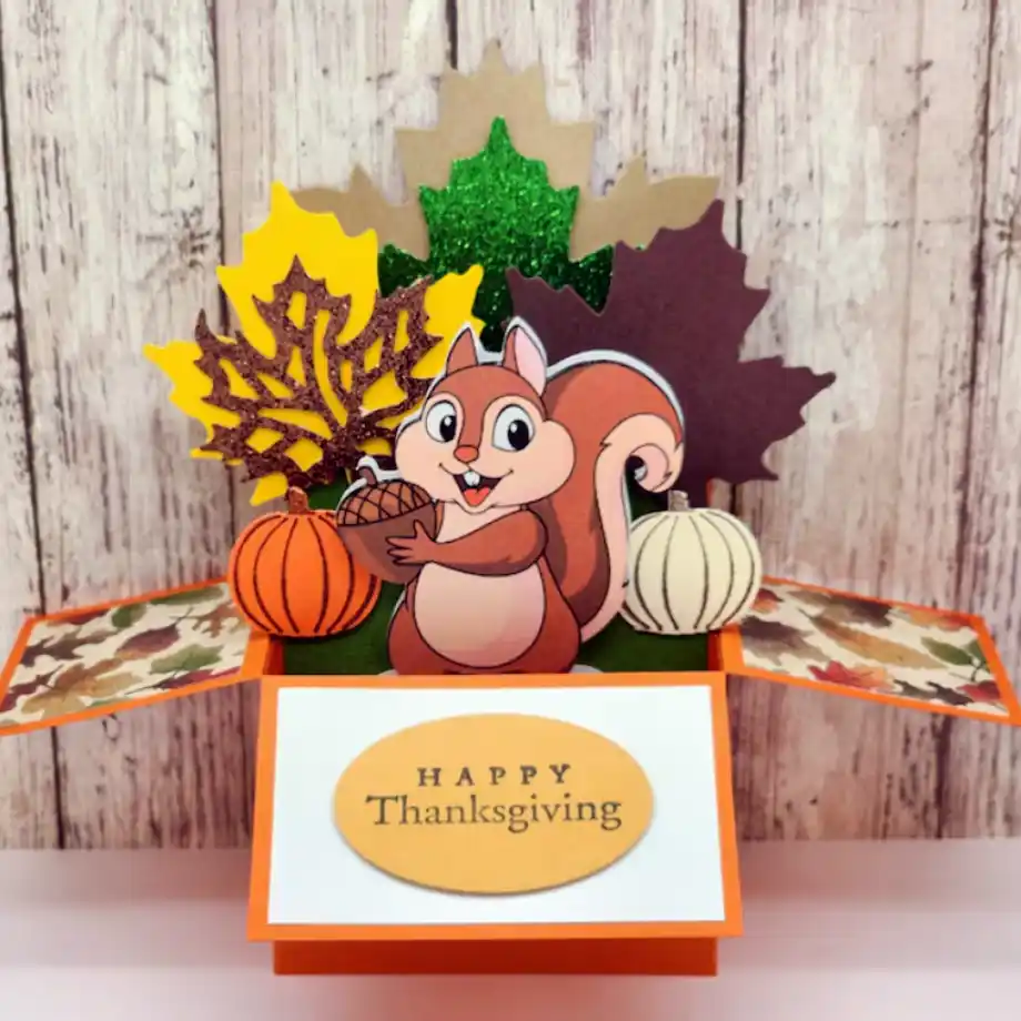 A festive pop-up card featuring a cheerful squirrel holding an acorn, surrounded by colorful fall leaves, pumpkins, and a "Happy Thanksgiving" message on the card. Perfect for sharing happy thanksgiving messages with loved ones.