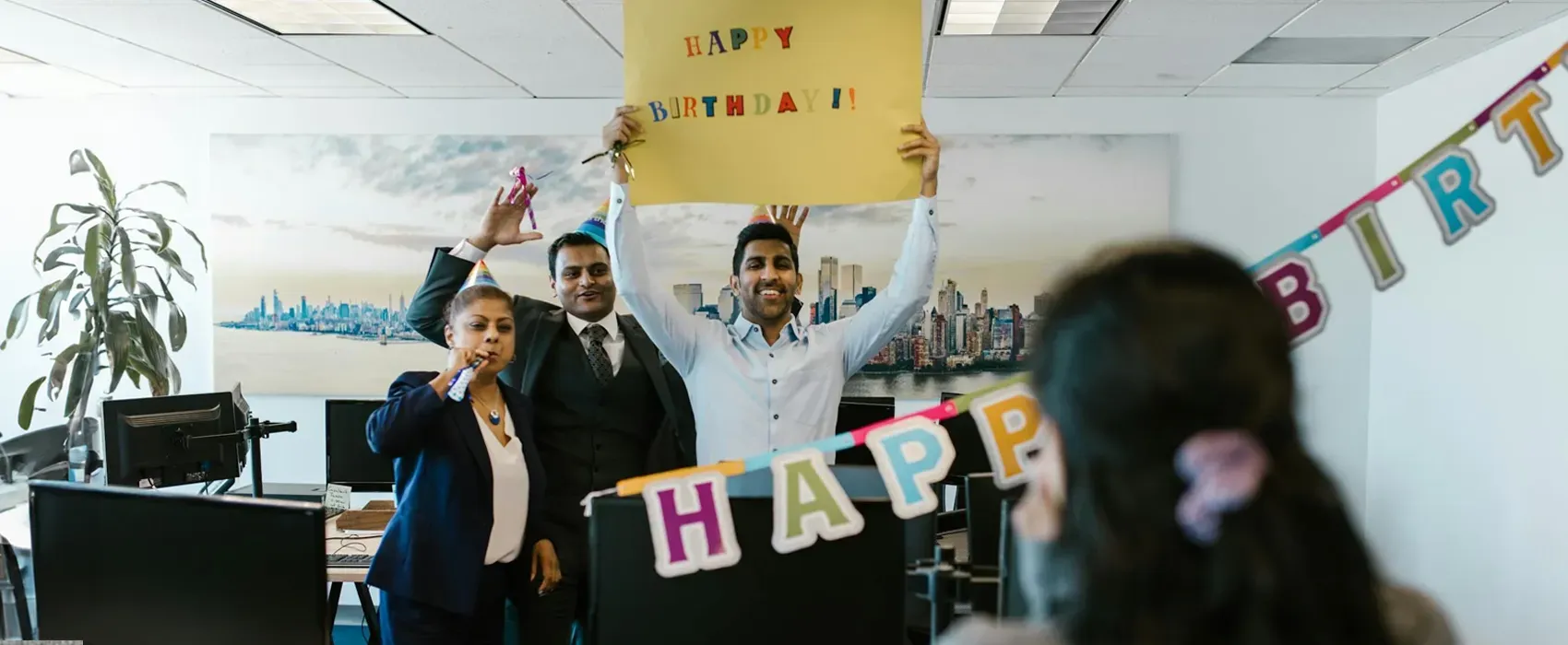 Office colleagues holding a 'Happy Birthday' sign and decorations to celebrate a coworker’s birthday, creating a cheerful atmosphere with birthday wishes for a coworker.