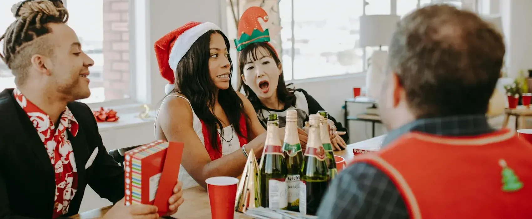 A group of friends enjoying a holiday party, wearing festive hats and sharing laughter while playing a game involving Christmas trivia questions, with bottles of sparkling drinks and colorful decorations on the table.