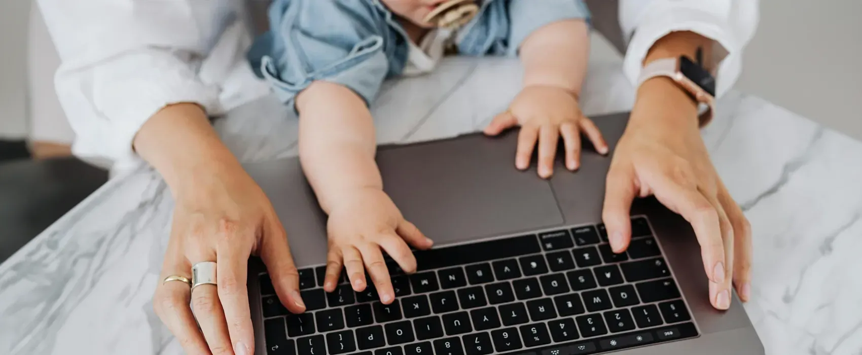 A mom typing on a laptop with her Gen Beta baby reaching for the keyboard, showcasing multitasking and modern parenting.