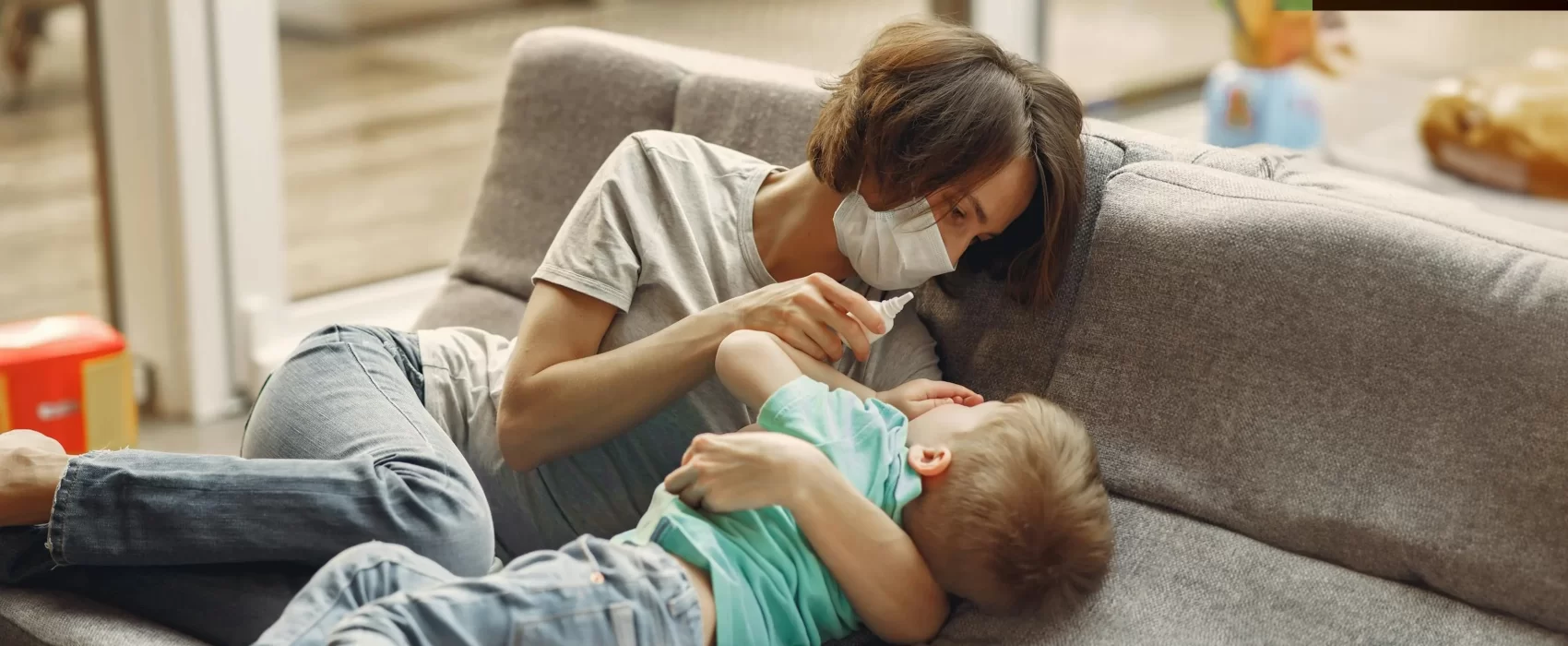 A mother wearing a protective mask taking care of her sick child on a couch, showing warmth and comfort, conveying a heartfelt get well soon message.