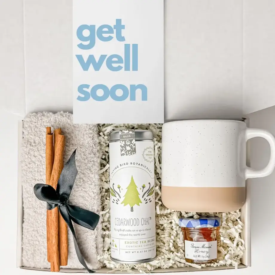 A comforting get well soon gift box containing a mug, cedarwood chai tea, cinnamon sticks, jam, and a cozy towel, paired with a cheerful "get well soon" card.