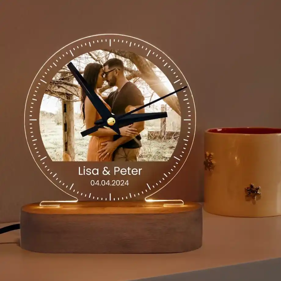  A custom LED clock with a photo of a couple embracing, engraved names Lisa and Peter, and the date 04.04.2024, set on a wooden base.