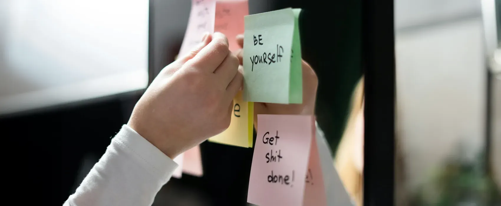 A close-up image of a person holding white and pink sticky notes with motivational hard work quotes, symbolizing productivity and dedication in the workplace.