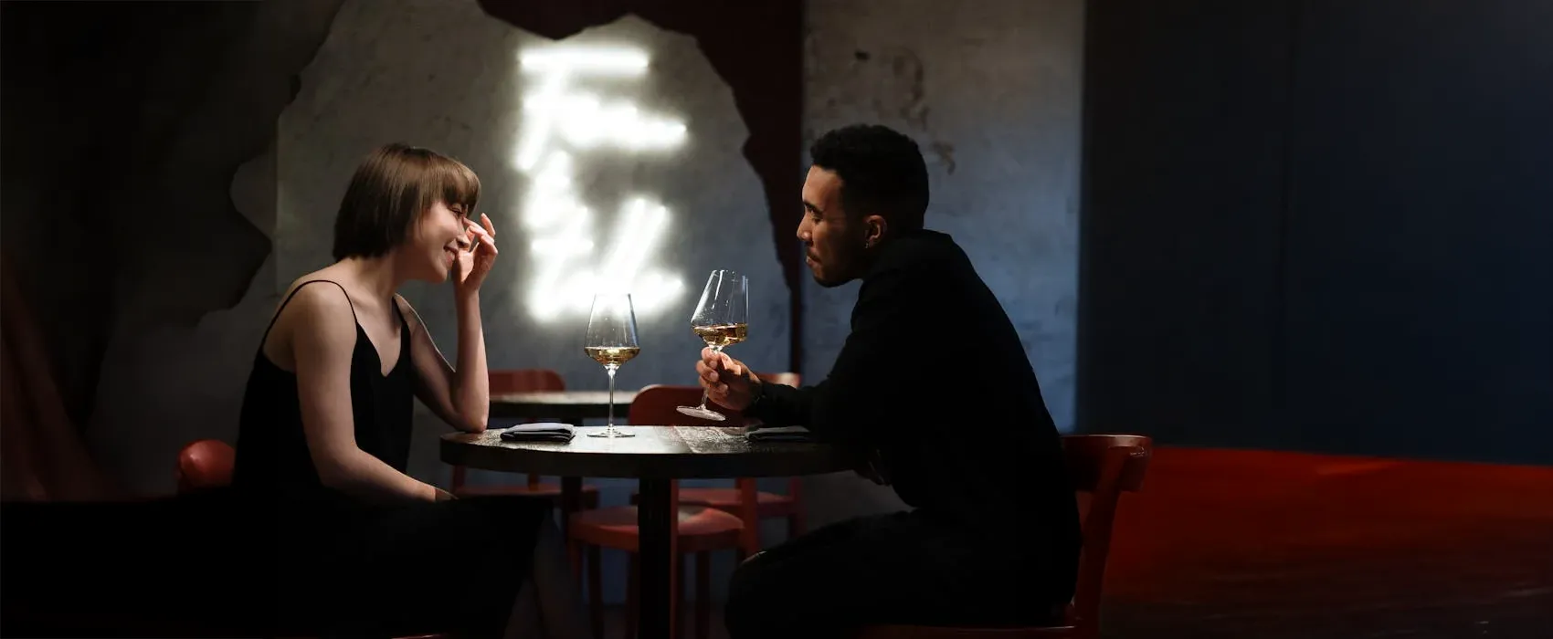 A couple sitting at a table in a dimly lit restaurant, sharing wine and engaging in deep conversation, illustrating questions to ask your girlfriend for a meaningful connection.