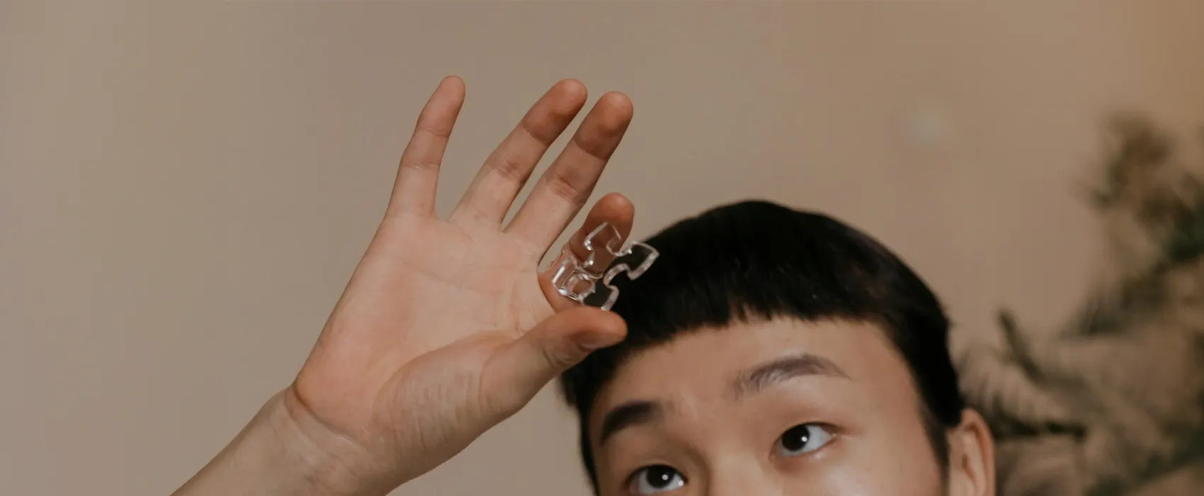 A person holding a transparent puzzle piece against a neutral background, symbolizing the thought-provoking and challenging nature of riddles for adults.