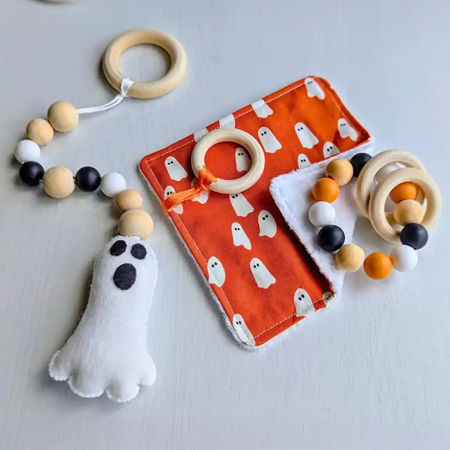 Set of Halloween-inspired baby toys, including a ghost plush with a wooden teething ring, a spooky bead bracelet, and a ghost-patterned cloth — the perfect festive touch for your little one's boo basket.