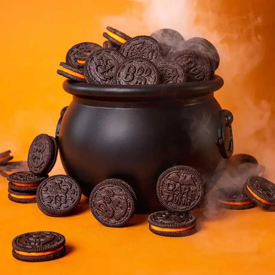 A black cauldron overflowing with spooky-themed chocolate sandwich cookies, featuring Halloween designs like "Boo" and spiderwebs, with festive orange filling—perfect for adding a magical touch to any Halloween boo basket.