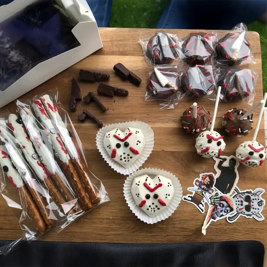 A chilling assortment of Halloween-themed treats, including chocolate-dipped pretzel sticks with bloody designs, Jason Voorhees-inspired cupcakes, spooky cake pops, and creepy chocolate weapons — the perfect spooky-sweet combo for a Halloween boo basket.