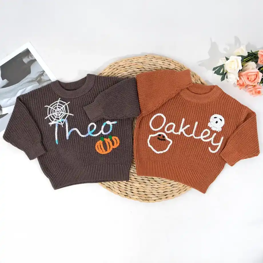 Two cozy, personalized Halloween-themed sweaters for kids, one brown with "Theo" and a pumpkin design, the other orange with "Oakley" and a ghost motif — perfect, festive gifts to include in a Halloween boo basket for a spooky and stylish celebration.