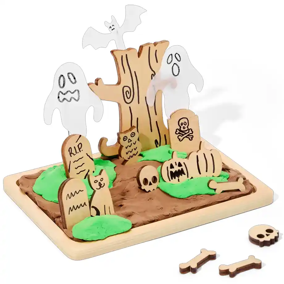 A Halloween-themed playdough graveyard kit featuring wooden cutouts of tombstones, ghosts, a haunted tree, a bat, and spooky creatures. The set includes brown and green playdough for a creepy cemetery scene, making it a fun and creative addition to any kid’s boo basket for Halloween.