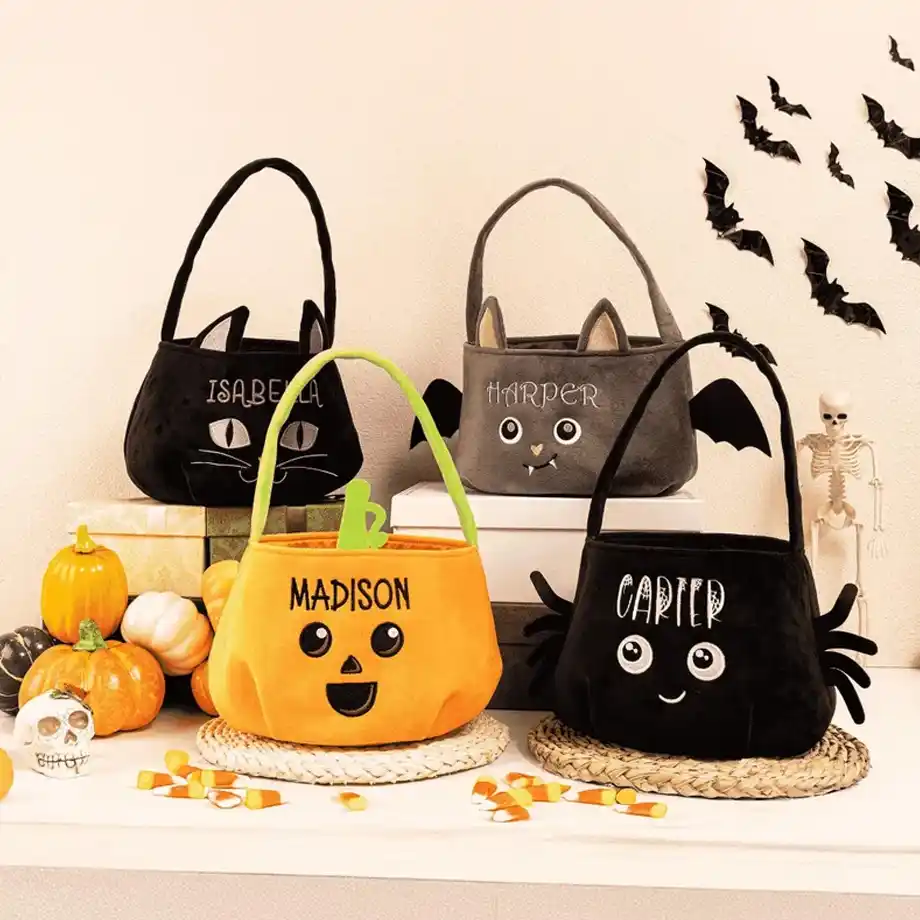 A set of four personalized boo baskets designed as a pumpkin, black cat, bat, and spider, displayed with Halloween decorations like pumpkins, candy corn, and bat wall decals.