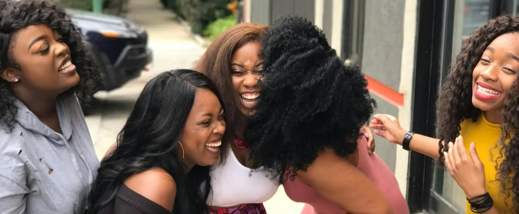 A group of four women laughing together outdoors, sharing a moment of happiness and friendship.