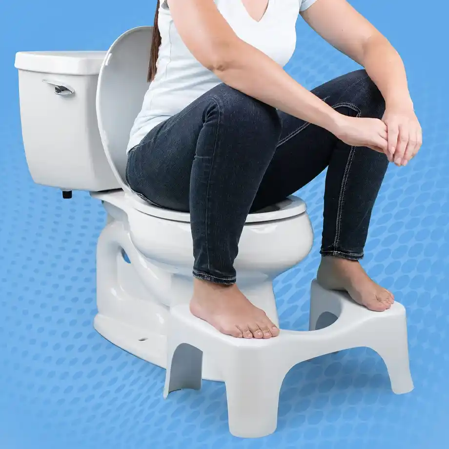 A person using a white toilet stool while sitting on a toilet, demonstrating a squatting position for better posture and improved bathroom ergonomics. The background features a blue pattern. This functional yet humorous item makes a great choice for white elephant gift ideas, combining health benefits with a touch of comedy.