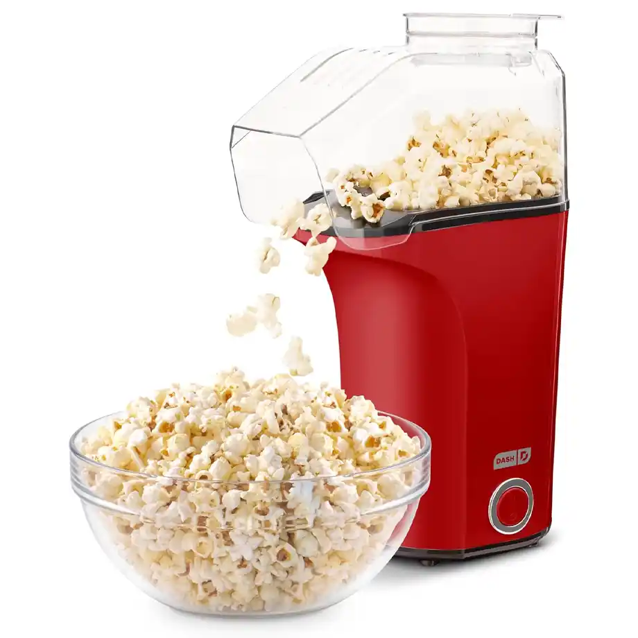 A red Dash hot air popcorn maker popping fresh popcorn into a glass bowl, making it a fun and practical option for white elephant gift ideas. A perfect gift for movie lovers and snack enthusiasts.