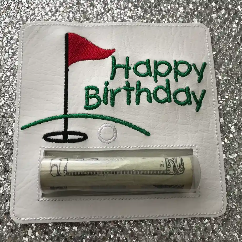 A golf-themed Happy Birthday money holder with embroidered text, a red flag, and a putting green design. Features a clear pocket to hold cash, making it a fun and practical golf gift idea.